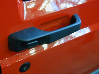 IMAGE: A door handle on the outside of a Jeep. The handle is shaped so that it must be grasped first, then a small button pushed with one thumb, and finally the entire handle must be pulled in order to open the door.